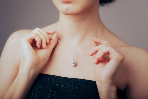 Woman wearing elegant teardrop silver pendant necklace, black strapless dress, jewelry close-up.