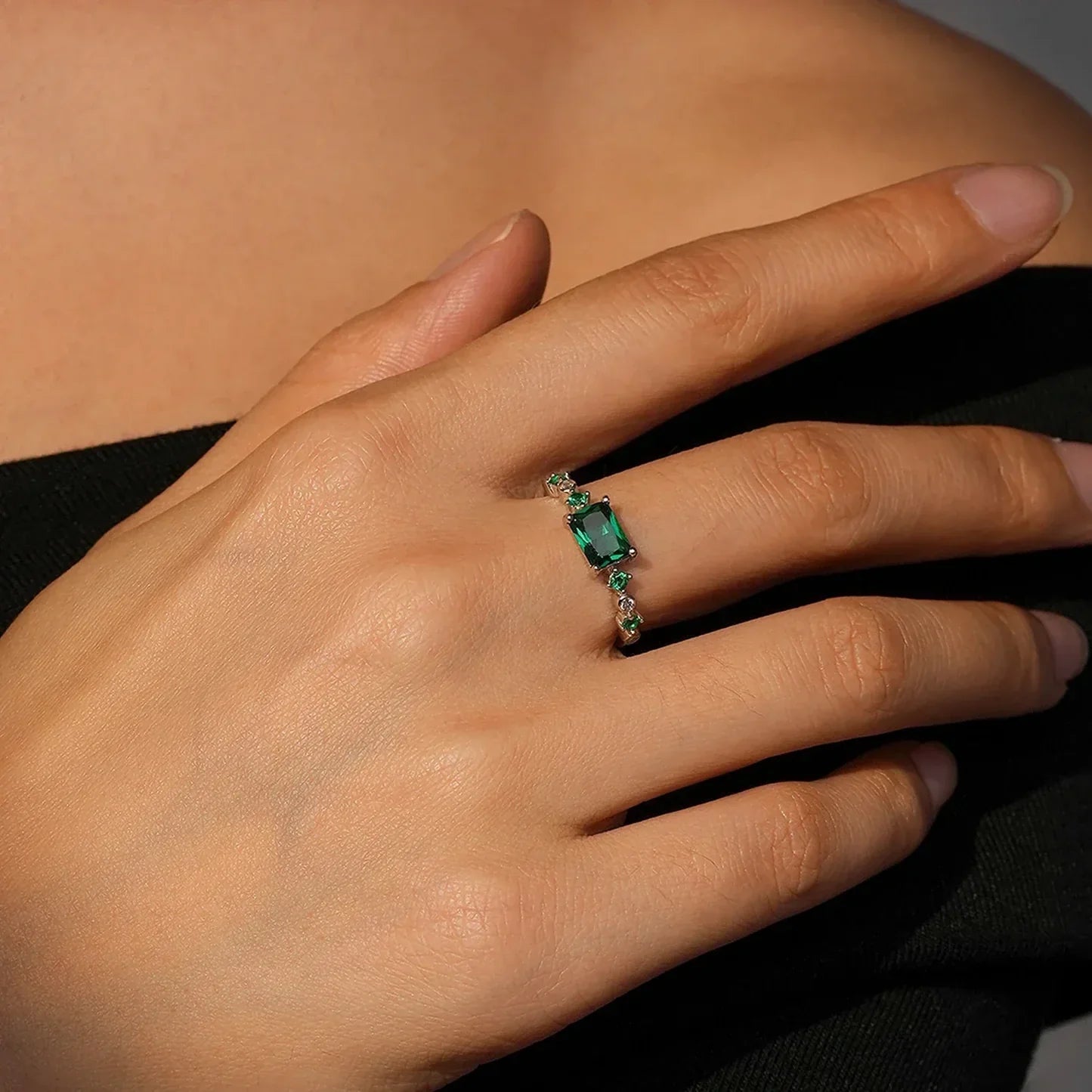 Hand wearing a silver ring with a green emerald-cut gemstone and clear accents