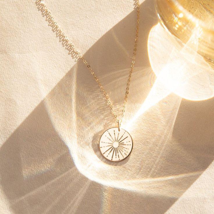 Gold-plated sunburst pendant necklace on a textured surface with sunlight reflections