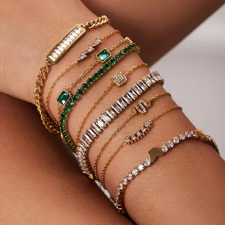 A delicate stack of gold chains and pearl bracelets from the TM & Co. Jewels collection, styled against natural foliage.