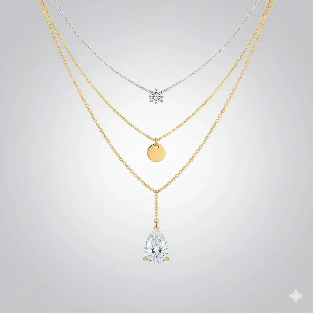 Layered gold and silver necklaces with round and teardrop pendants on a light background