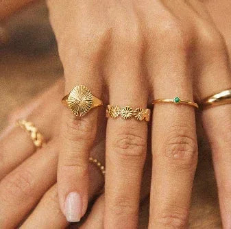 Hand wearing multiple 18K gold-plated rings with unique, elegant designs on natural background