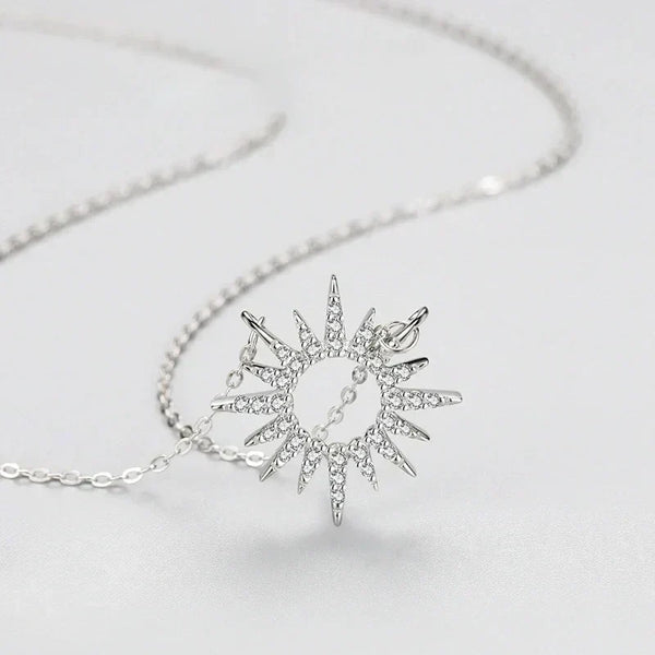 Silver sun-shaped pendant on a chain against a light gray background