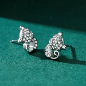 Silver cat-shaped earrings with gemstones on a green textured surface