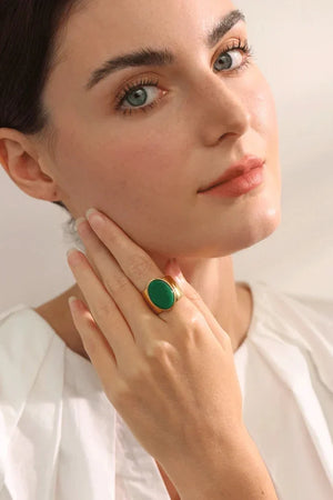 Woman wearing a green ring on her finger with a plain background