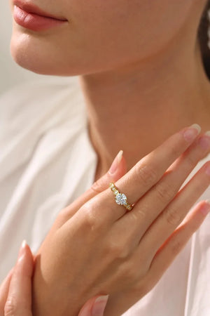 Close-up of a hand wearing a gold ring with a diamond on a neutral background