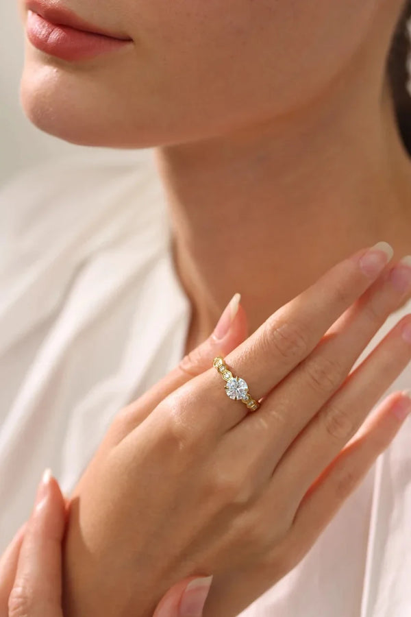 Close-up of a hand wearing a gold ring with a diamond on a neutral background
