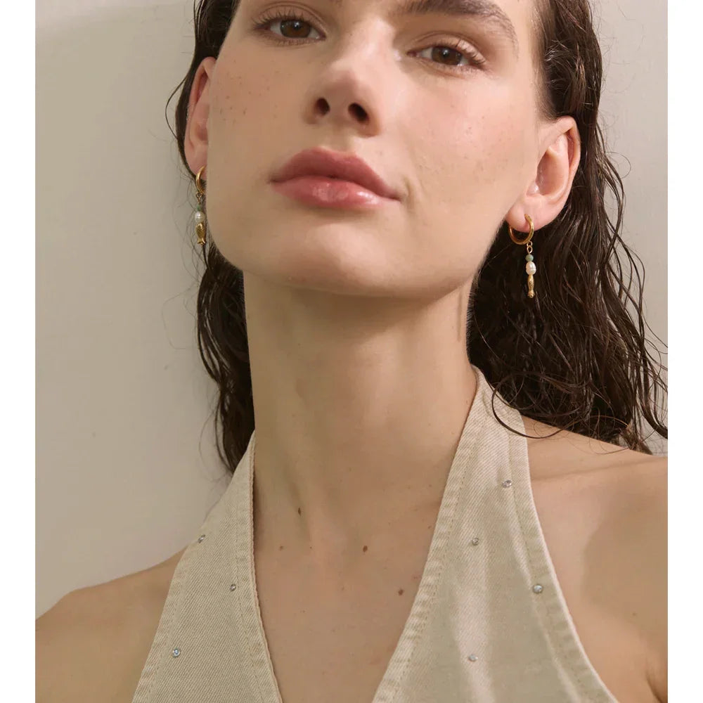 Close-up of a woman wearing gold earrings with pearls against a neutral background