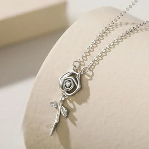 Silver rose-shaped pendant necklace on a beige surface