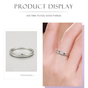 Silver ring with small diamonds on a gray background and worn on a finger.