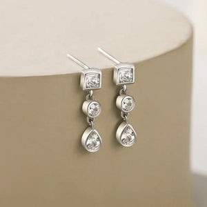 Silver earrings with clear gemstones on a beige surface