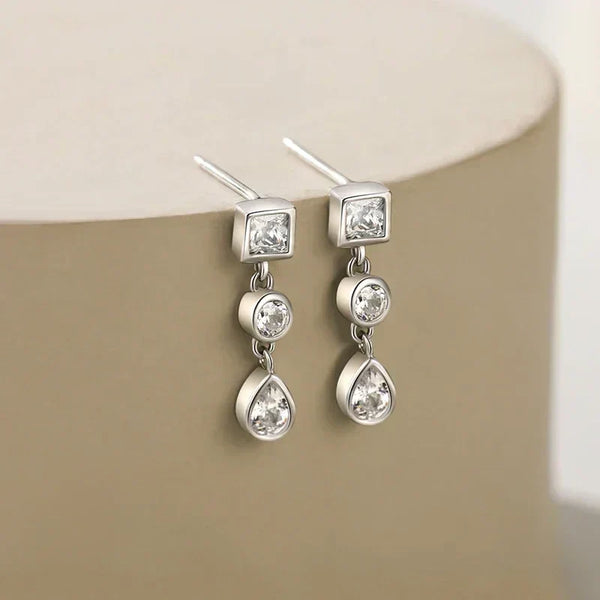 Silver earrings with clear gemstones on a beige surface