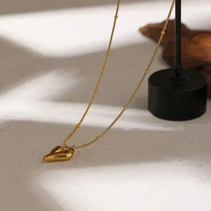 18K gold-plated heart pendant necklace with beaded chain on light stone surface