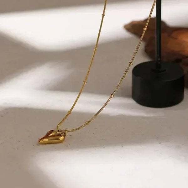 18K gold-plated heart pendant necklace with beaded chain on light stone surface