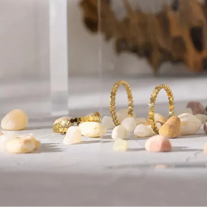 Gold-plated silver textured rings on white stones, minimalist jewelry display