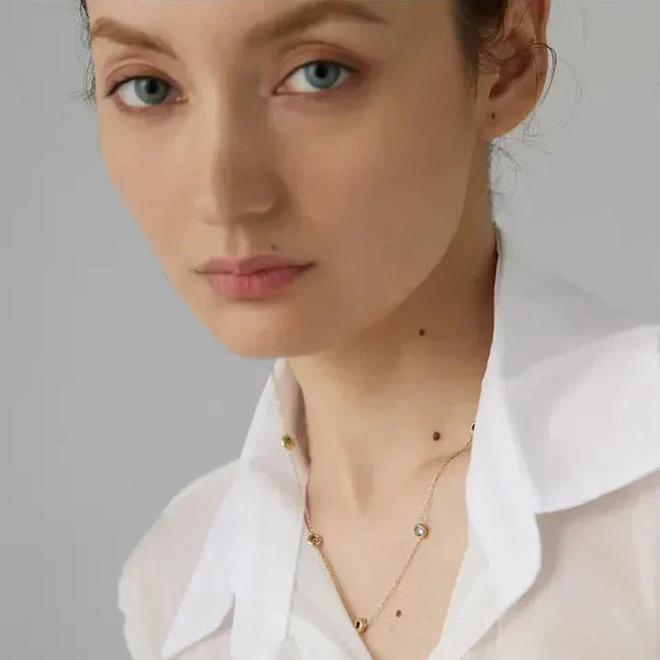 Woman wearing delicate 18K gold-plated necklace with gemstone accents, white collared shirt