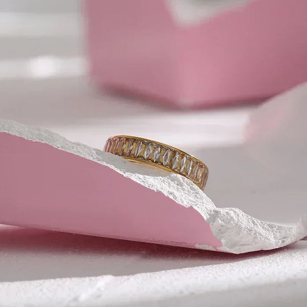Gold-plated ring with baguette-cut crystals on a pink and white textured surface