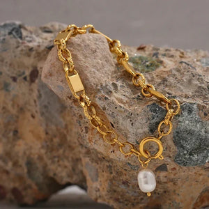 Gold bracelet with a pearl charm on a textured stone surface