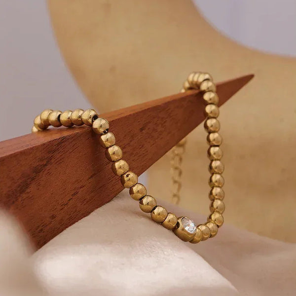 18K gold-plated beaded bracelet with single clear gem on geometric display
