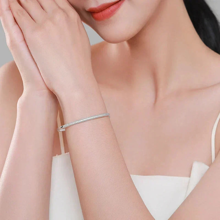 Woman wearing a silver bracelet on a neutral background.