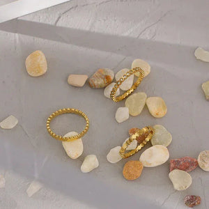 Gold-plated textured stacking rings displayed on smooth stone pebbles and concrete.