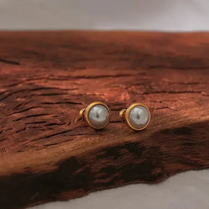 Pair of gold-plated pearl stud earrings on rustic wood surface