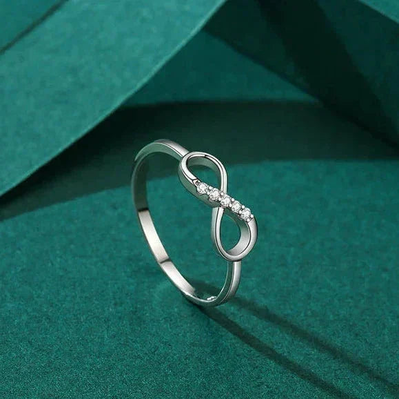 Silver infinity ring with small diamonds on a teal fabric background