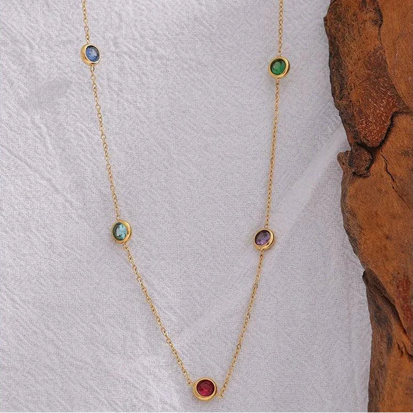 18K gold-plated necklace with multicolored gemstone stations on a white textured background