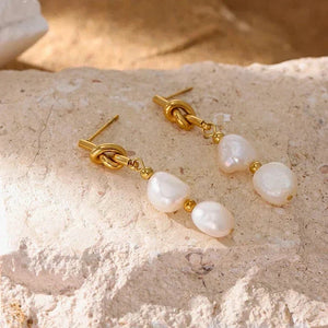 Pearl and gold knot earrings on a textured surface