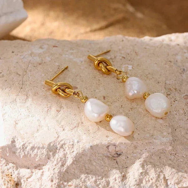 Pearl and gold knot earrings on a textured surface