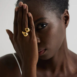 Woman wearing unique gold-plated statement ring on hand, in white pleated dress