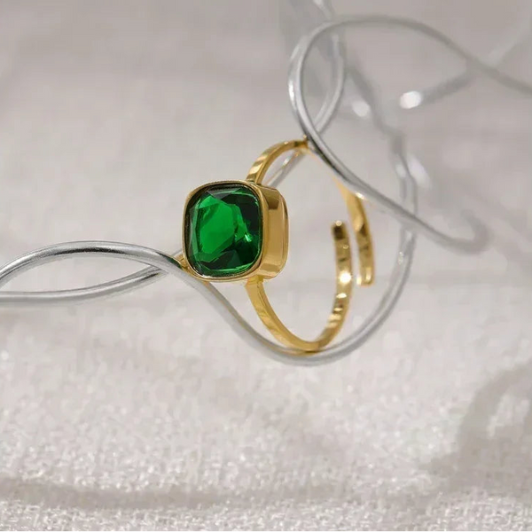 Gold-plated ring with square green gemstone displayed on textured surface