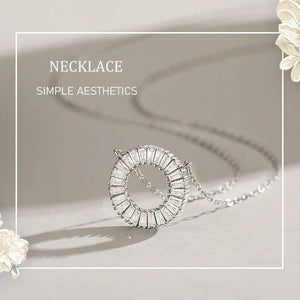 Silver necklace with a circular pendant on a light background, surrounded by white flowers.