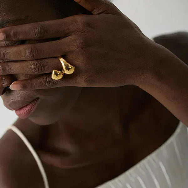 Woman wearing a gold-plated statement ring, hand covering face, in a white dress