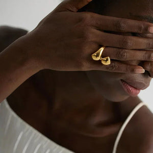 Woman wearing unique gold-plated statement ring on hand, in white pleated dress