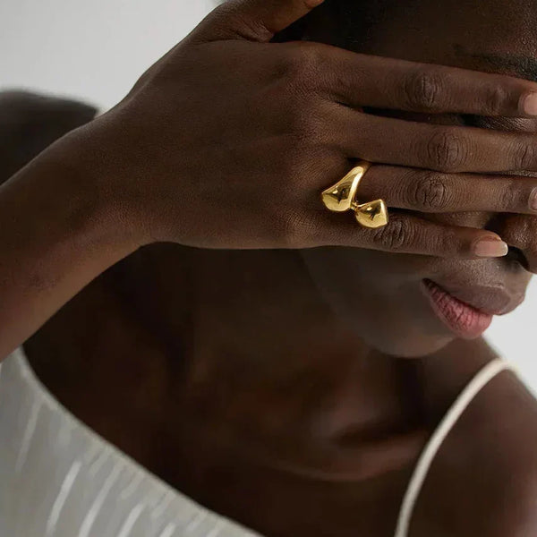 Woman wearing unique gold-plated statement ring on hand, in white pleated dress