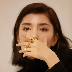 Woman in black sweater wearing multiple gold rings, including pearl and heart designs, on her hand
