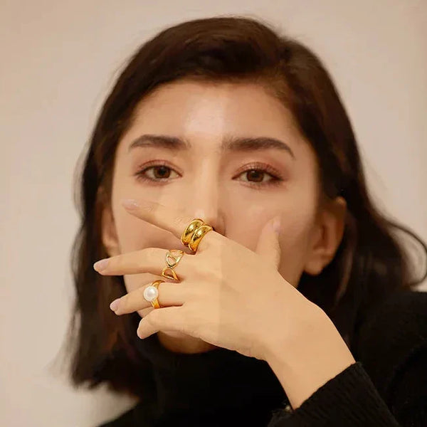Woman in black sweater wearing multiple gold rings, including pearl and heart designs, on her hand