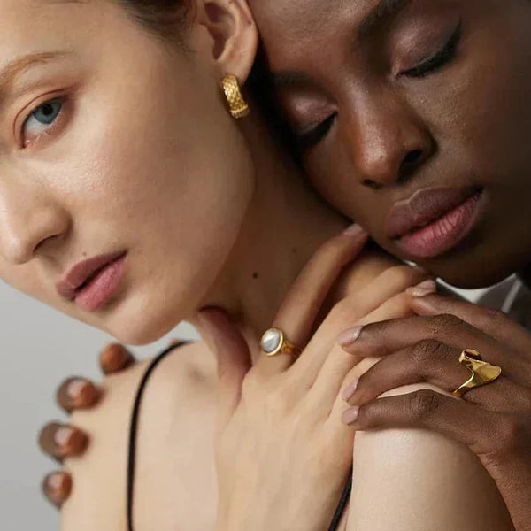 Two women showcasing gold-plated earrings and rings with elegant minimalist design.