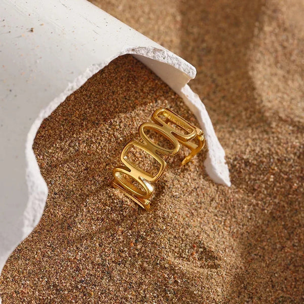 18K gold-plated open ring with geometric design displayed on sandy surface