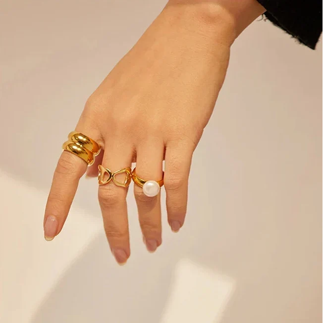 Woman in black sweater wearing multiple gold rings, including pearl and heart designs, on her hand