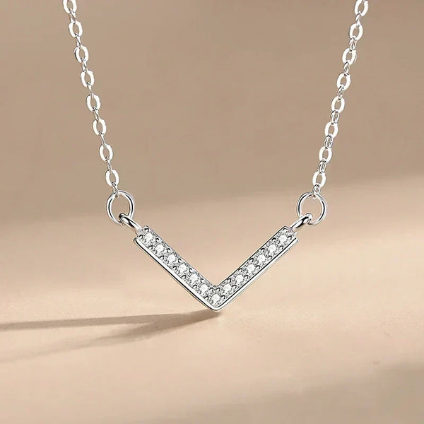 Prism Glow Pendant - TM & CO. JEWELS -Silver V-shaped necklace with small crystals on a beige backgroundز