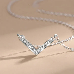 Silver V-shaped necklace with clear stones on a beige background.