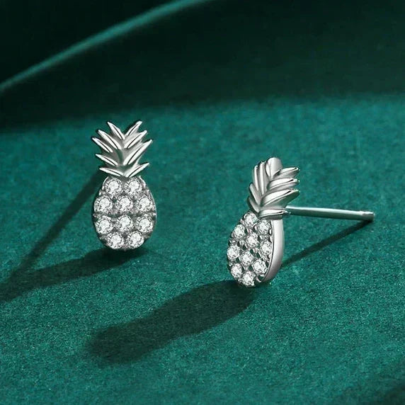 Silver pineapple earrings with gemstones on a teal surface