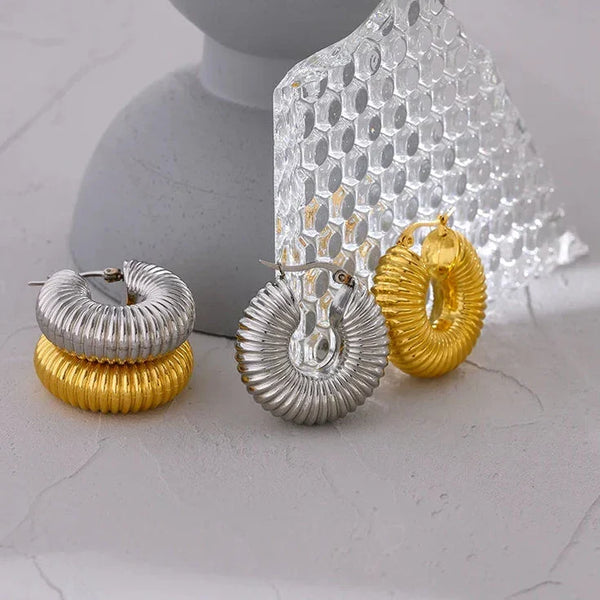 Set of gold and silver earrings on a white surface with a gray stand.