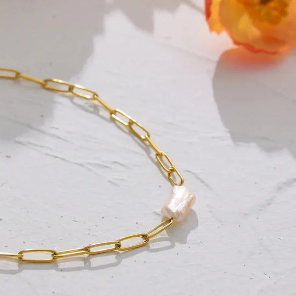 Gold chain necklace with a pearl pendant on a light surface with a flower in the background