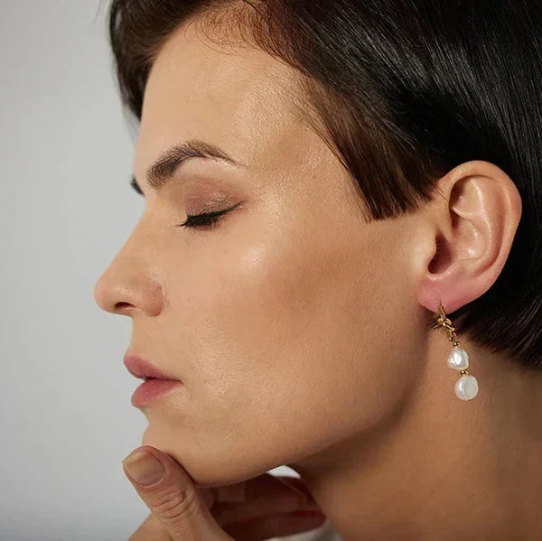Close-up of a woman wearing a gold earring with a white stone on a neutral background