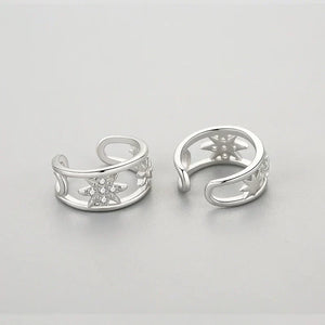Pair of silver open earrings with star designs on a light gray background