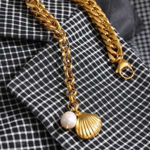 Gold chain bracelet with shell and pearl charms on a checkered fabric background