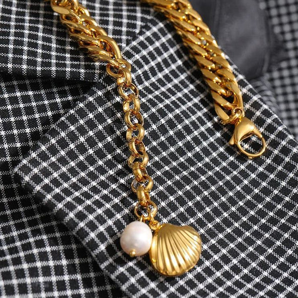Gold chain bracelet with shell and pearl charms on a checkered fabric background